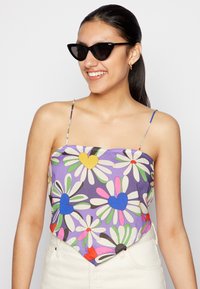 Top com estampado floral colorido e corações, apresentando alças finas e uma bainha diagonal, feito de tecido leve. O modelo usa óculos de sol pretos em formato de gato.