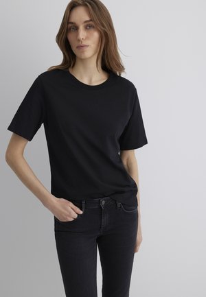Schwarzes Baumwoll-T-Shirt mit kurzen Ärmeln und rundem Halsausschnitt, kombiniert mit dunklen Jeans, die eine lockere Passform und eine glatte Textur zeigen.