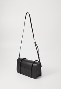 Bolsa de ombro em couro negro com forma retangular, apresentando uma textura suave, acentuada por duas alças curvas e uma alça longa ajustável.