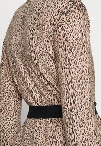 Sukienka w panterkę z beżowym tłem i czarno-rdzawymi plamkami, z długimi rękawami i czarnym elastycznym paskiem w talii, podkreślającym sylwetkę.