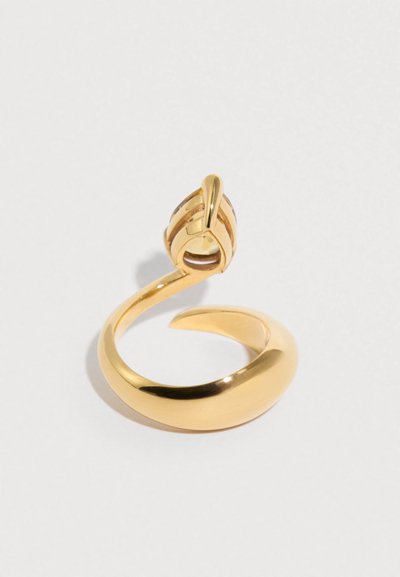 Χρυσής απόχρωσης μεταλλικό δαχτυλίδι με λείο, στρογγυλεμένο δακτύλιο και σπειροειδή σχεδίαση με μια λεπτή λεπτομέρεια στην κορυφή που μοιάζει με ευαίσθητο κόμπο.