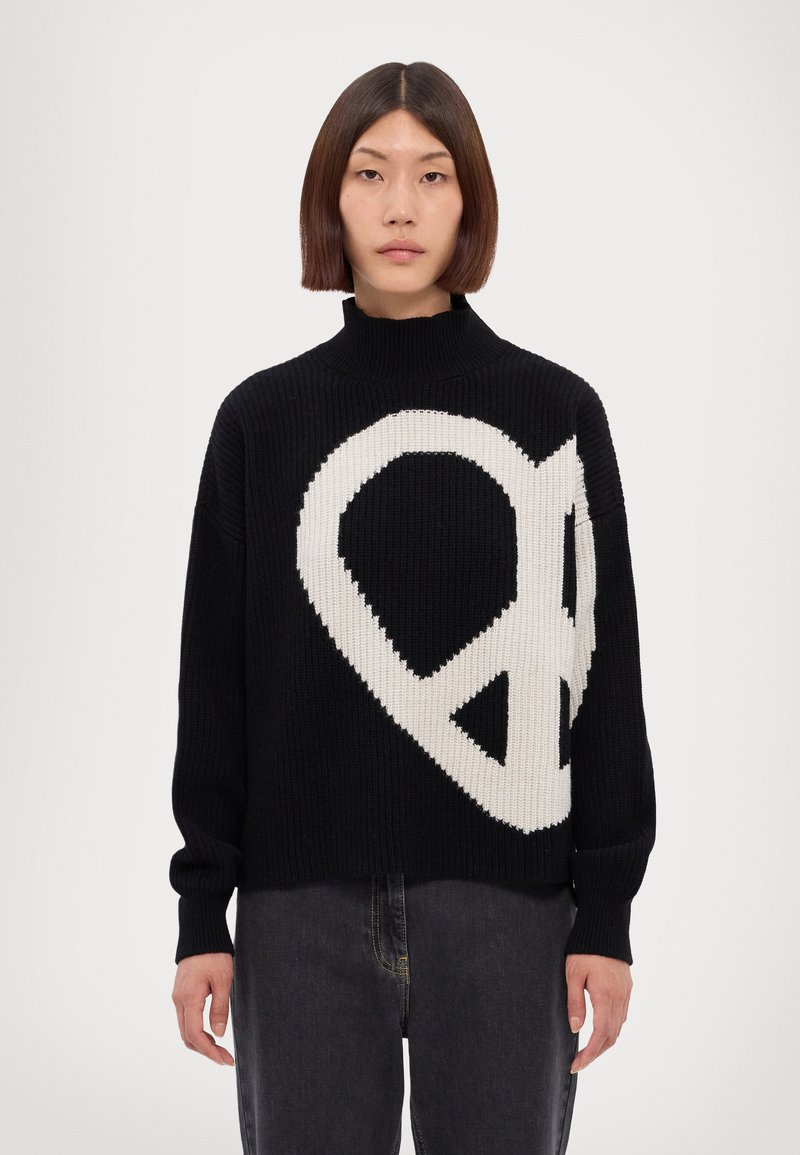Schwarzer Strickpullover mit einem großen weißen Friedenssymbol-Graphic auf der Vorderseite. Hoher Kragen und lange Ärmel, mit lockerer Passform.