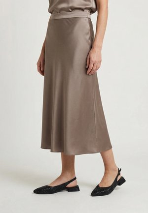 Taupekleurige satijnen midi-rok met hoge taille gecombineerd met zwarte lage hakken geweven slingback schoenen bij een staand persoon.