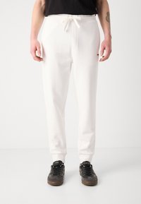 Hvide joggerbukser med snor i taljen, der har sidelommer og ribbet afslutning. Bæres med sorte sneakers, hvilket skaber kontrast.