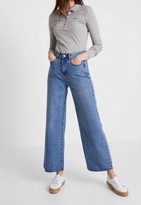 Light gray long-sleeve polo shirt with collar, high-waisted blue wide-leg jeans, and white sneakers with a jute sole.