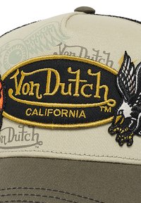 Gorra beige y oliva con un logo bordado en negro y dorado de Von Dutch California, que presenta un águila bordada sosteniendo una rama.