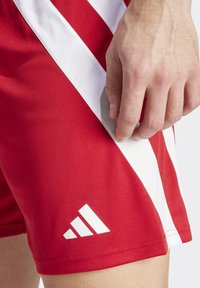 Rote Sportshorts mit weißen diagonalen Streifen und einem Adidas-Logo in der unteren rechten Ecke. Glattes, leichtes Material mit einer figurschmeichelnden Passform.