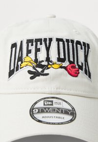 White cap with adjustable strap featuring embroidered "DAFFY DUCK" text, yellow and red cartoon character accents, and a round New Era label.