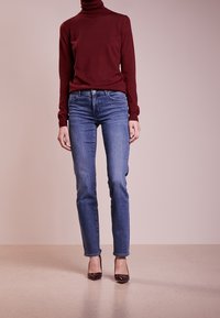 Burgunderfärgad polotröja, blå skinny jeans och mörka lackskor. Slät tyg, åtsittande design och klassisk stil.