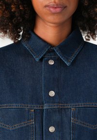 Donkerblauwe denimjack met drukknoopjes, een gespreide kraag en contrasterende oranje stiksels; beschikt over borstzakken en een gestructureerde stof.
