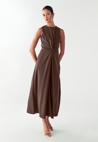 Vestido marrón sin mangas con un detalle anudado en la cintura, tela fluida y un dobladillo de longitud media. Textura suave y diseño minimalista.