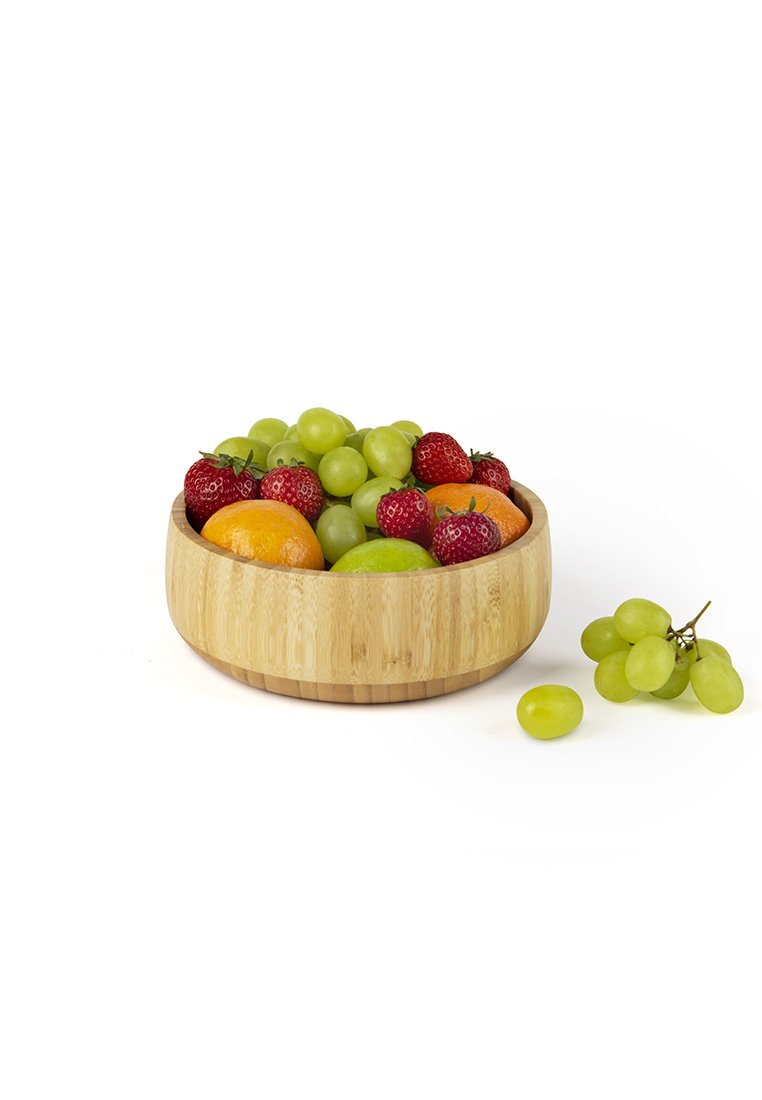 Eine Bambusschüssel mit einer glatten Oberfläche, die grüne Trauben, Erdbeeren und eine Orange enthält. Zusätzlich liegen grüne Trauben neben der Schüssel.