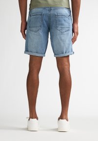 Pantalones cortos de mezclilla en azul claro con puños enrollados, cuentan con dos bolsillos traseros y un ajuste relajado. Combinados con zapatillas blancas.