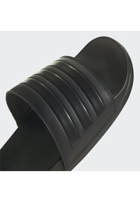 Black slide sandal with three horizontal grooves on the strap, textured upper, and rounded toe. Lightweight synthetic material, sleek design.