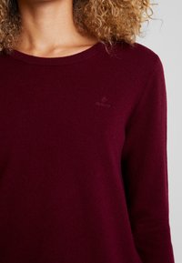 Pullover a maglia bordeaux con scollatura rotonda. Presenta un logo discreto sul petto e una texture morbida. Maniche lunghe, design aderente.