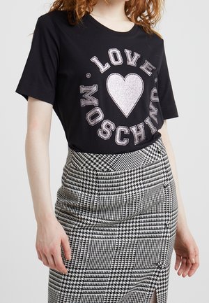 T-shirt en coton noir avec un texte métallique "LOVE" et un motif cœur, associé à une jupe crayon à motif pied-de-poule en noir et blanc.
