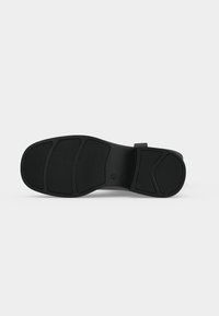Semelle en caoutchouc noir avec des patins de grip texturés segmentés, talon plat et une section de voûte légèrement relevée, présentée sur un fond uni.