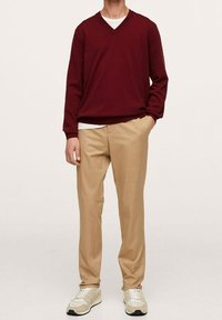 Pull en maille col V marron associé à un T-shirt crème et un pantalon beige. Tissu lisse, coupe décontractée, et des baskets neutres complètent le look.