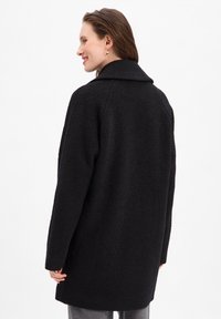 Manteau en laine noire avec un design structuré, grand col et tissu texturé. Doté de longues manches et d'une coupe légèrement oversize.