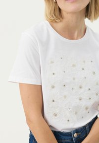T-shirt en coton blanc avec broderies florales agrémentées de perles. Col ras du cou, manches courtes et coupe décontractée.