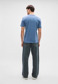 Ανοιχτό μπλε κοντομάνικο μπλουζάκι συνδυασμένο με φαρδιά σκούρα τζιν. Το μπλουζάκι έχει απλό σχέδιο και στρογγυλή λαιμόκοψη.