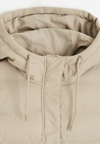 Beżowa kurtka pikowana z wysokim kołnierzem, regulowanymi sznurkami, gładką powierzchnią i minimalistycznym designem. Brak widocznych elementów metalowych lub wzorów.