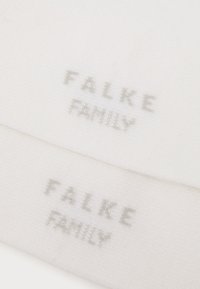 Tessuto bianco con la scritta "FALKE FAMILY" in grigio chiaro. La texture appare morbida e lavorata a maglia, con due strati visibili.