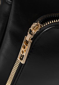 Dettaglio della cerniera di una borsa in pelle nera, con un lucchetto dorato lucido, superficie testurizzata e accenti dorati a contrasto lungo il binario della cerniera.