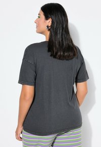 Ciemnoszary t-shirt z krótkim rękawem o luźnym kroju, z widocznymi detalami szwów i miękką fakturą, noszony z prążkowanymi spodniami piżamowymi.