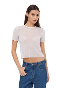 Cropped top bianco a maniche corte realizzato in materiale trasparente, adornato con perline e paillettes. Abbinato a jeans in denim blu a vita alta.