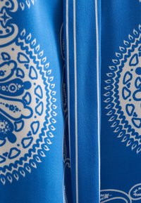 Tessuto blu a motivo con intricati disegni bianchi, con una trama liscia e sottili strisce bianche a contrasto lungo i bordi.