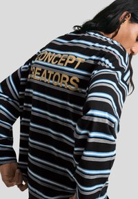 Fekete hosszú ujjú csíkos ing kék és fehér csíkokkal. A hátsó részen arany színű "CONCEPT CREATORS." felirattal. Puha anyagból készült.
