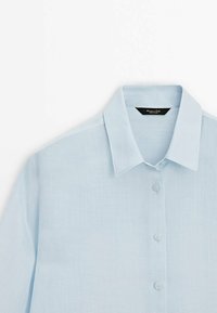 Himlens blå linneskjorta med spetsig krage, framknappar och lång ärm. Slät textur med avslappnad passform.