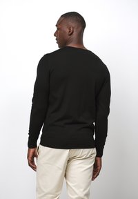 Svart långärmad tröja gjord av ett slätt, stickat material med rund halsringning, figurnära design och ribbade manschetter och nederkant.