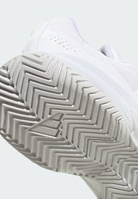 Biała sportowa podeszwa buta z zygzakowatym wzorem bieżnika i teksturowaną powierzchnią, z trójkątnym logo na boku.