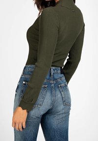 Olijfgroene geribbelde top met lange mouwen en een nekkraag, gecombineerd met vervaagde blauwe high-waisted jeans met klassieke achterzakken en versleten accenten.