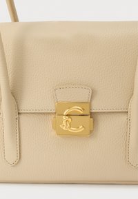 Beige handtas van gestructureerd leer met een gouden rechthoekige sluiting waarop een verweven C- en S-logo te zien is op de voorflap.