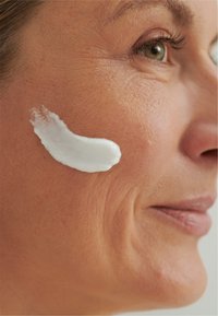 White cream is applied to the cheek of a person with light skin; visible texture and wrinkles are present on the skin.