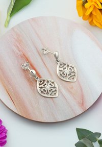 Söta silverörhängen med intrikata utskurna blommönster, hängande från en rund krok, visade på en marmorerad rund yta.