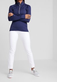 Marinfärgad atletisk kvartzip-top med långa ärmar; slim fit. Matchas med vita slim-fit-byxor och grå sneakers med ett cirkulärt remmar detalj.