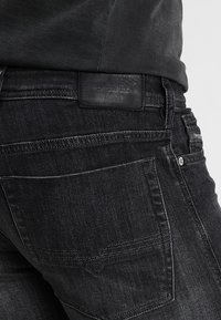 Jeans in denim nero con finitura testurizzata, dotati di un'etichetta in pelle sulla vita e un classico design a cinque tasche.