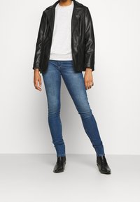 Blazer de cuero negro, sudadera gris clara, jeans ajustados azules, botines negros. El blazer tiene solapas con muesca; los jeans están bien ajustados.
