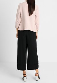 Chaqueta texturizada de color rosa claro, de manga tres cuartos, con un corte suelto, combinada con pantalones anchos negros y sandalias de tacón blancas.