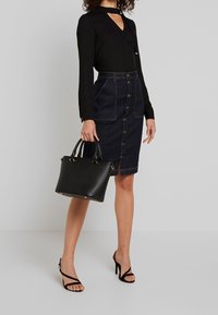 Svart långärmad topp med V-ringning och snörningsdetalj, kombinerad med en figurformad denimpennkjol med frontknappar och fickor. Svart handväska.