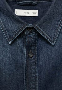 Dark blue denim shirt collar and buttons with visible MNG brand label and size information on tag inside collar.