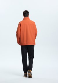 Orange waterproof jacket with a high collar, featuring a simple design. Paired with black pants and brown lace-up boots.