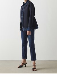 Mörkblå jacka med denimkrage, lager på lager över en denimskjorta, ihop med mörkblå jeans och svarta öppna klackar. Släta texturer.