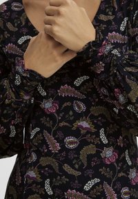 Langärmliges Kleid aus dunklem Stoff mit floralem Muster in Pink, Weiß und Grün; strukturiert mit gerafften Ärmeln und V-Ausschnitt.