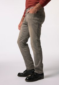 Jeans in denim grigio con vestibilità slim, caratterizzati da dettagli di cucitura laterale, tasche frontali e texture consumata. Abbinati a scarpe nere con lacci.