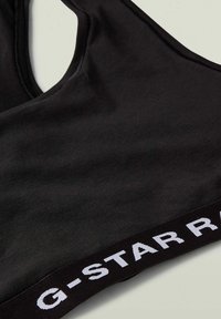 Črni športni modrček s širokim izrezom, izdelan iz gladkega materiala, z širokim elastičnim pasom, na katerem je v belem napisan "G-STAR RAW".